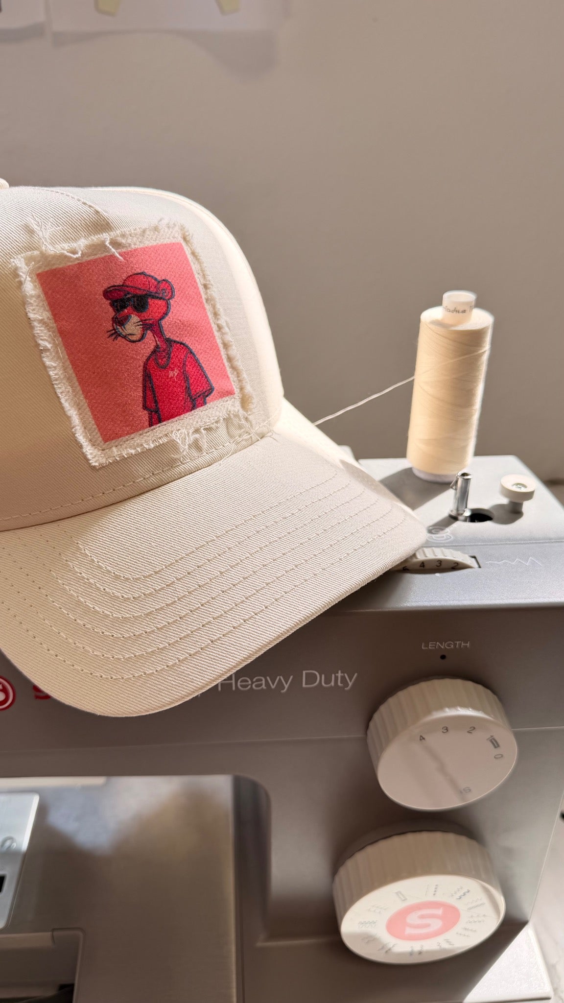 Cap mit aufgenähtem, ausgefranstem Stoffpatch neben Garn auf einer Nähmaschine