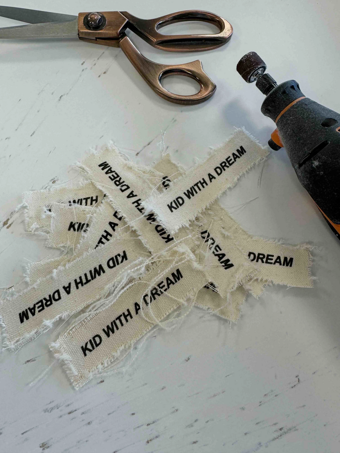 Ausgefranste Stoffpatches mit Textdruck auf dem Arbeitstisch neben Schere und Werkzeug